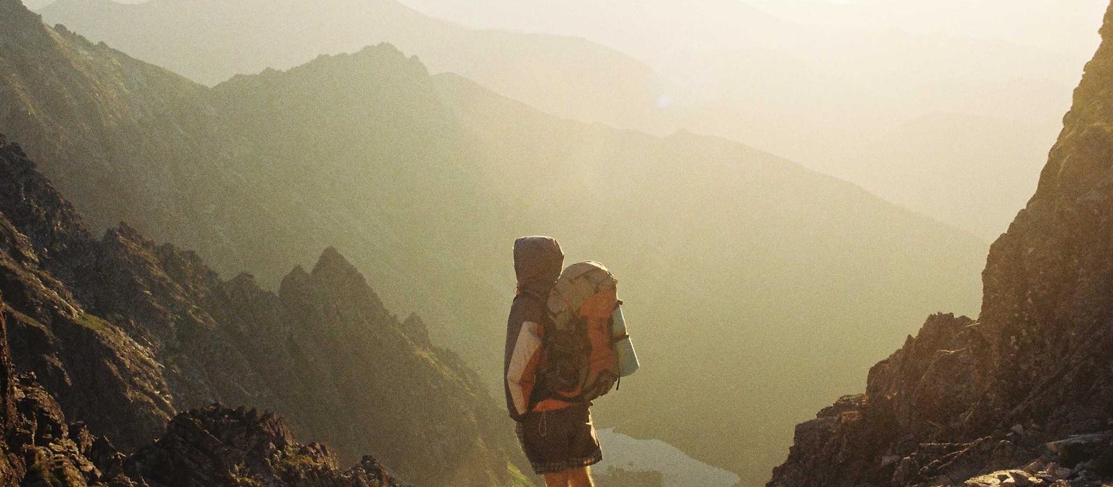 A hiker pausing on a golden mountain ridge at sunset